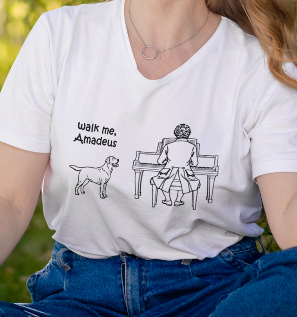A person wearing a white V-neck graphic T-shirt with a black line drawing of a Labrador Retriever and Mozart at a piano, plus the text 'walk me, Amadeus'. 