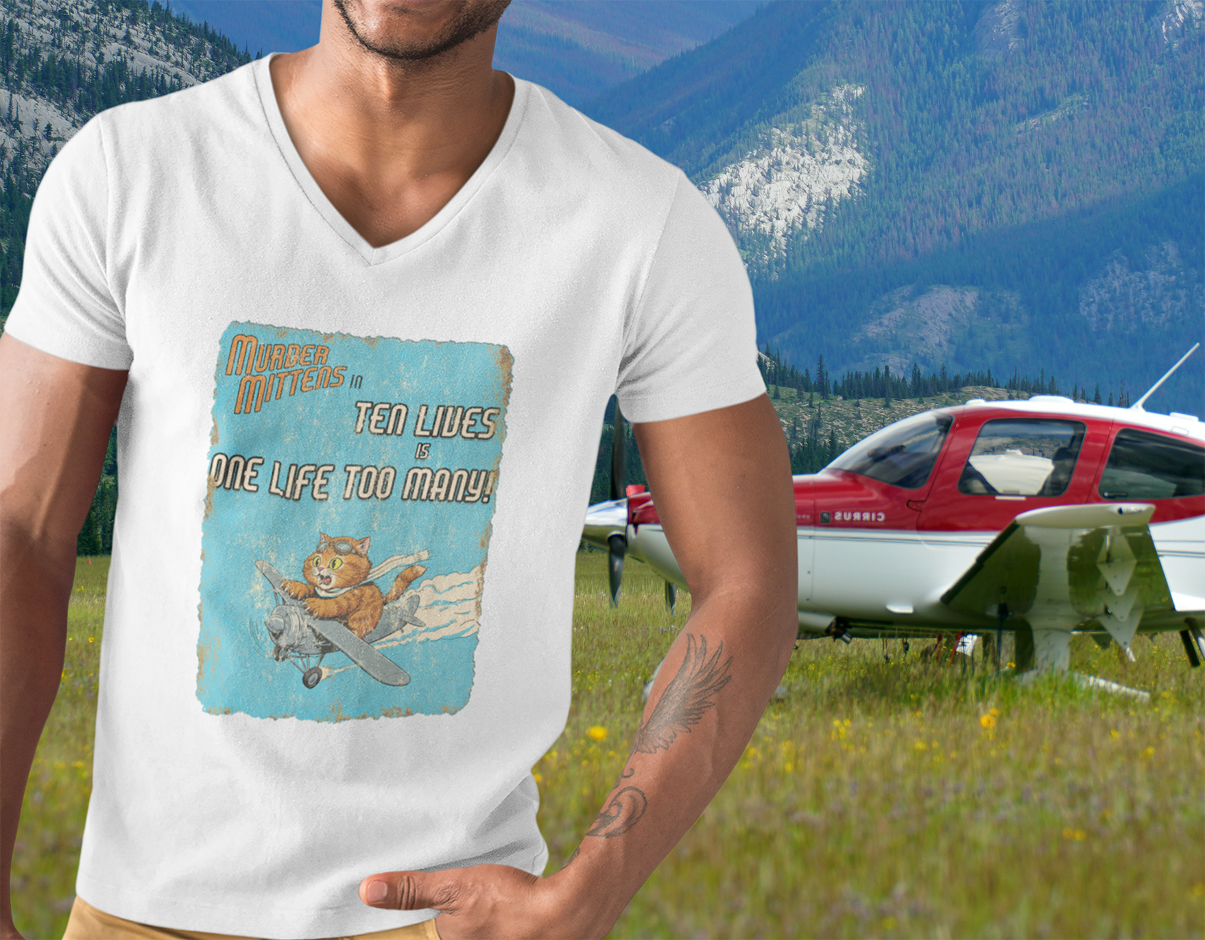 A man wearing a white V-neck t-shirt with a vintage-style graphic print of a cartoon cat flying a plane and the text 'Murder Mittens in Ten Lives is One Life Too Many!'.