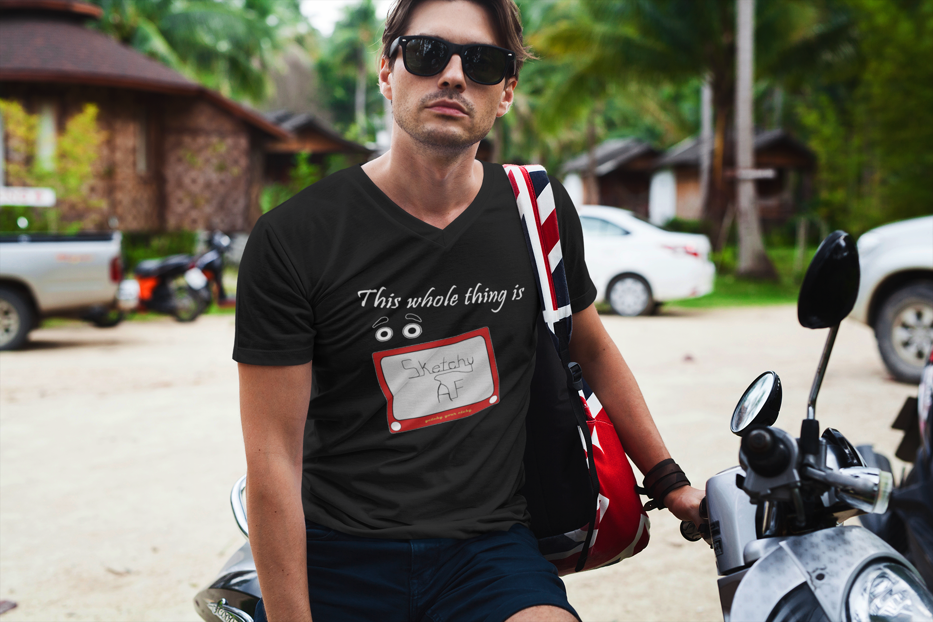 A man wearing a black v-neck t-shirt with the slogan, 'This whole thing is' above a pair of googly eyes, all above a retro red drawing toy with the words 'Sketchy AF' on the screen.