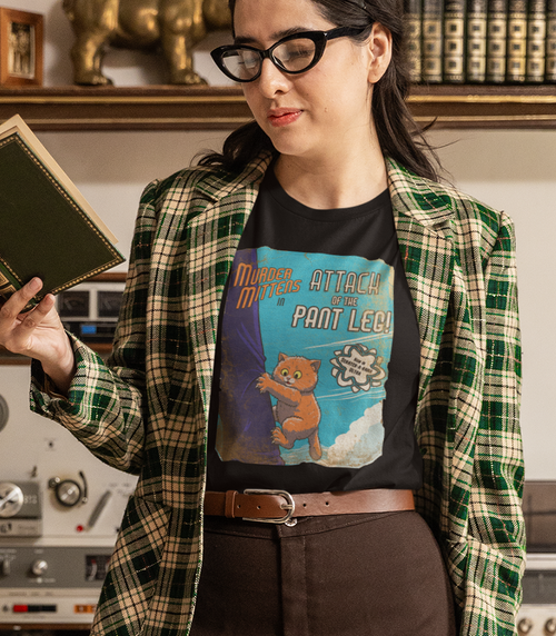 A woman wearing a black graphic t-shirt with a retro cartoon cat design, as the cat clings to an overly large pant leg. The caption reads, 'Murder Mittens in Attack of the Pant Leg!'