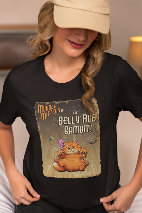 A woman wearing a black graphic t-shirt with a vintage-style print of an orange cat presenting his belly for a scratch, captioned 'Murder Mittens in the Belly Rub Gambit!'. 