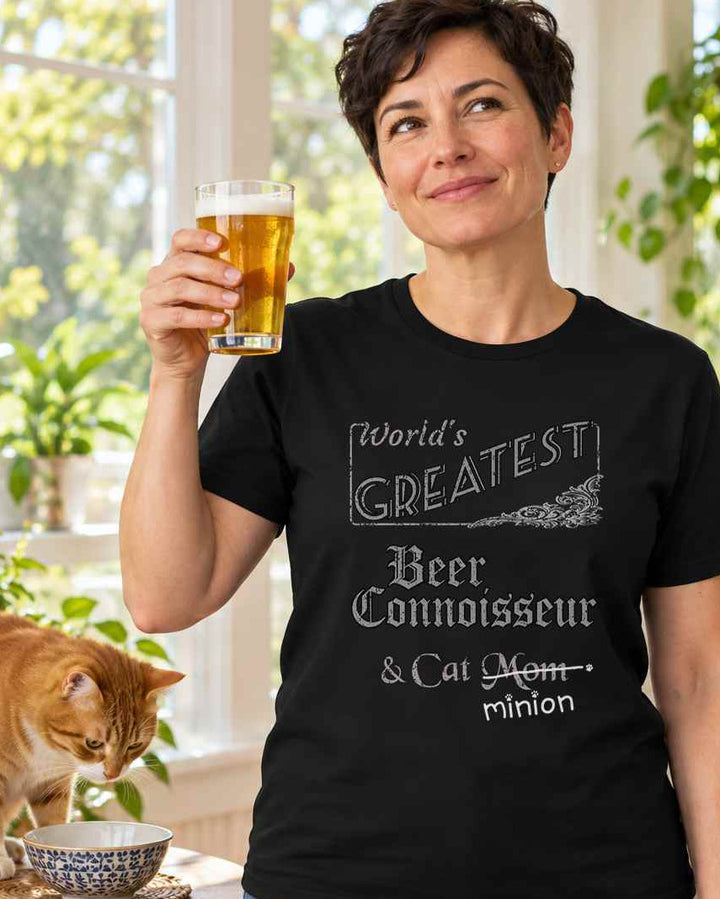 Woman raising a glass of beer beside a cat, wearing a black crew-neck t-shirt that reads, “World’s Greatest Beer Connoisseur & Cat Mom” with “Mom” crossed out and “minion” handwritten below with paw prints.