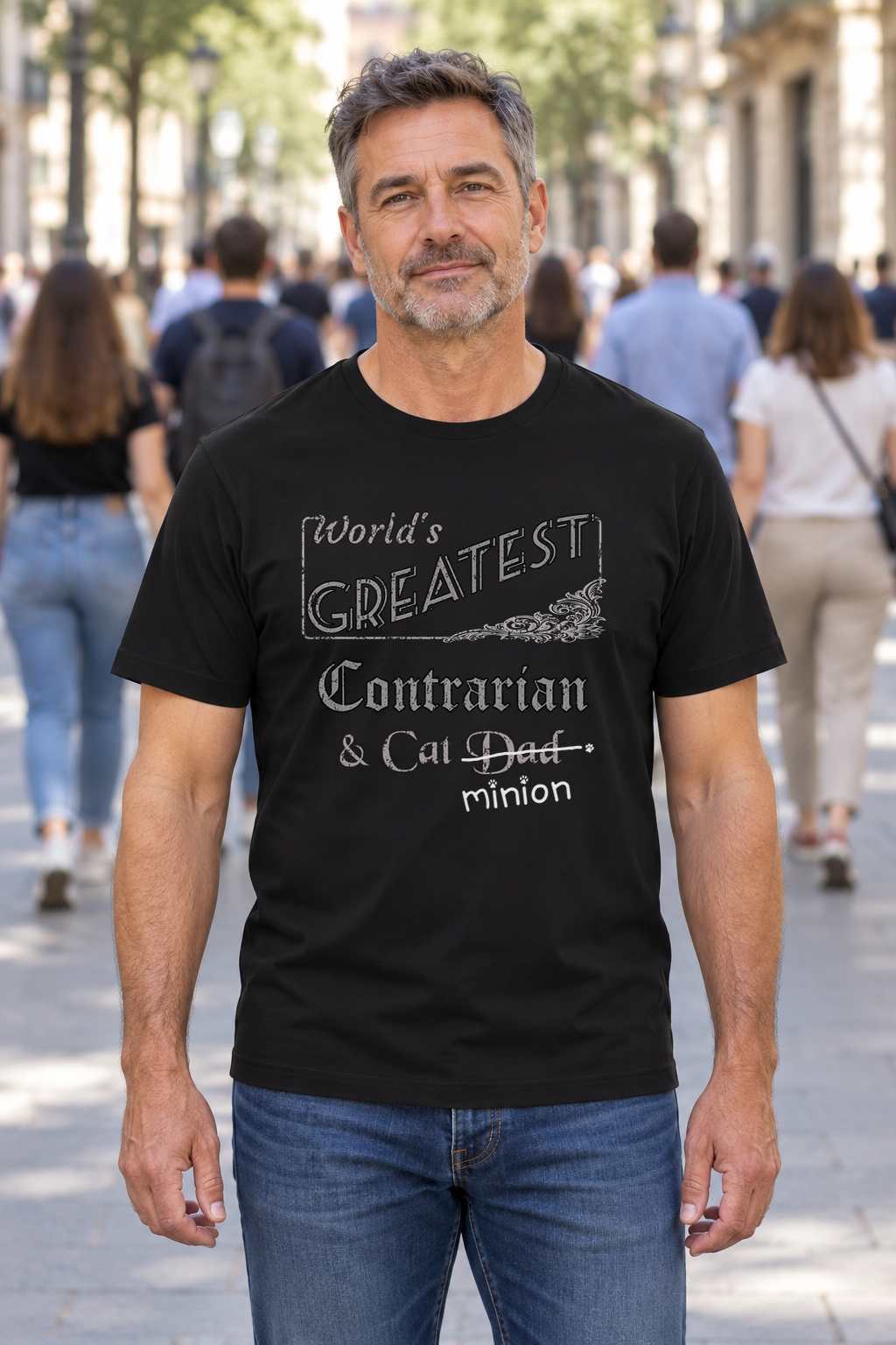 Man facing the camera while a crowd walks away, wearing a black crew-neck t-shirt that reads, “World’s Greatest Contrarian & Cat Dad” with “Dad” crossed out and “minion” handwritten below with paw prints.