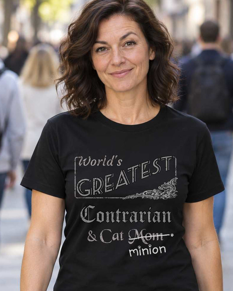 Woman facing the camera while a crowd walks away, wearing a black crew-neck t-shirt that reads, “World’s Greatest Contrarian & Cat Mom” with “Mom” crossed out and “minion” handwritten below with paw prints.