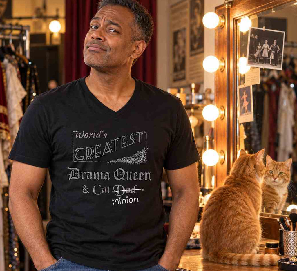 Man standing beside a cat in a pub, wearing a black V-neck T-shirt reading “World’s Greatest Drama Queen & Cat Dad.” “Dad” is crossed out, with “minion” handwritten beneath it and surrounded by cat paw prints.