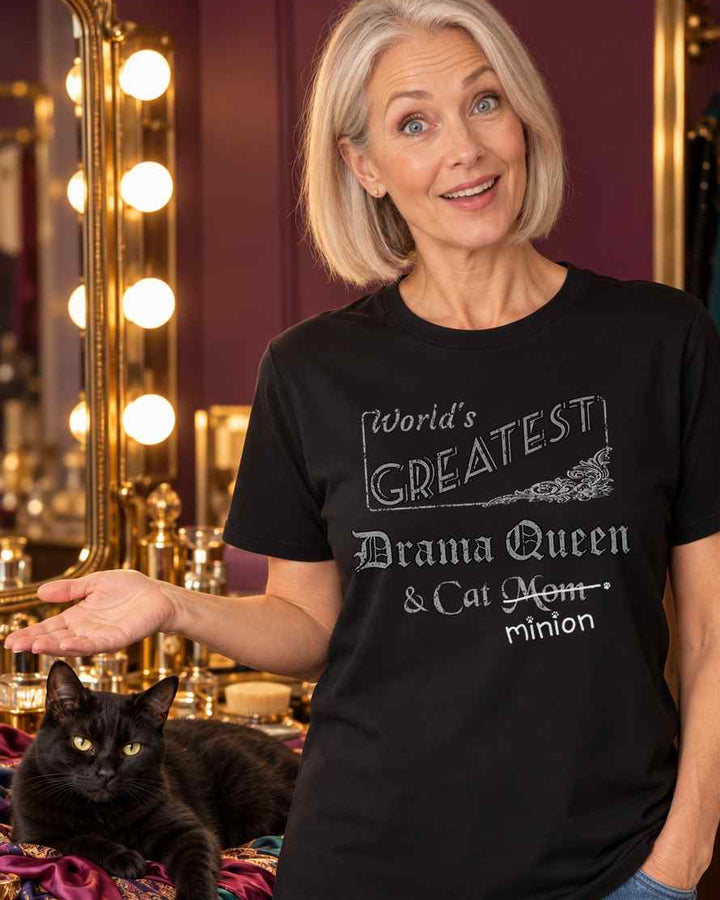 Woman presenting a cat sprawled across scarves in a dressing room, wearing a black crew-neck t-shirt that reads, “World’s Greatest Drama Queen & Cat Mom” with “Mom” crossed out and “minion” handwritten below with paw prints.
