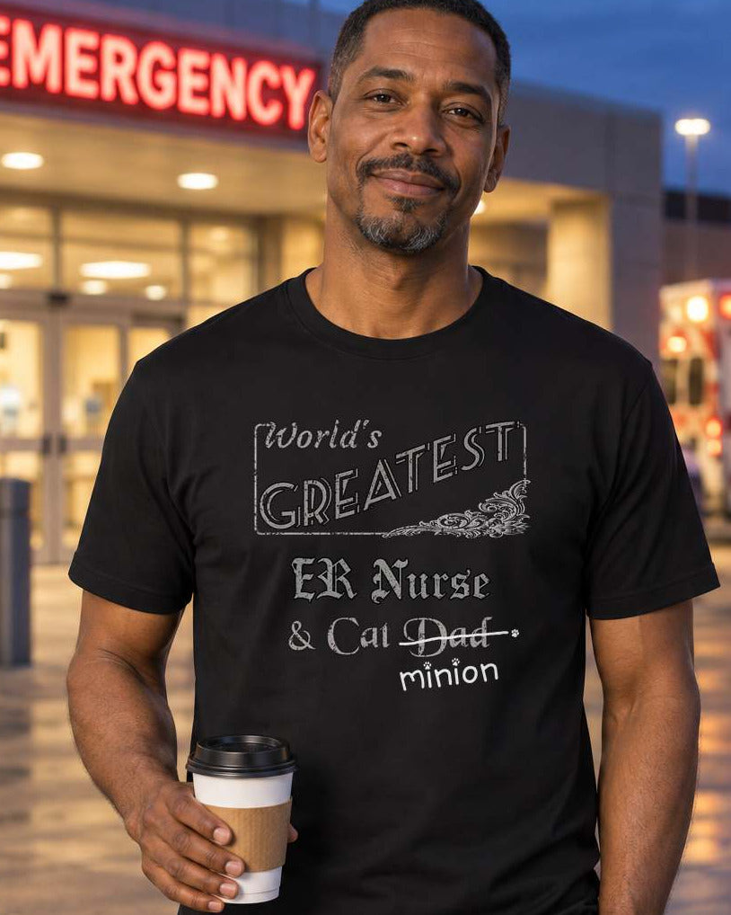 Man holding coffee outside a hospital emergency entrance at dusk, wearing a black crew-neck t-shirt that reads, “World’s Greatest ER Nurse & Cat Dad” with “Dad” crossed out and “minion” handwritten below with paw prints.