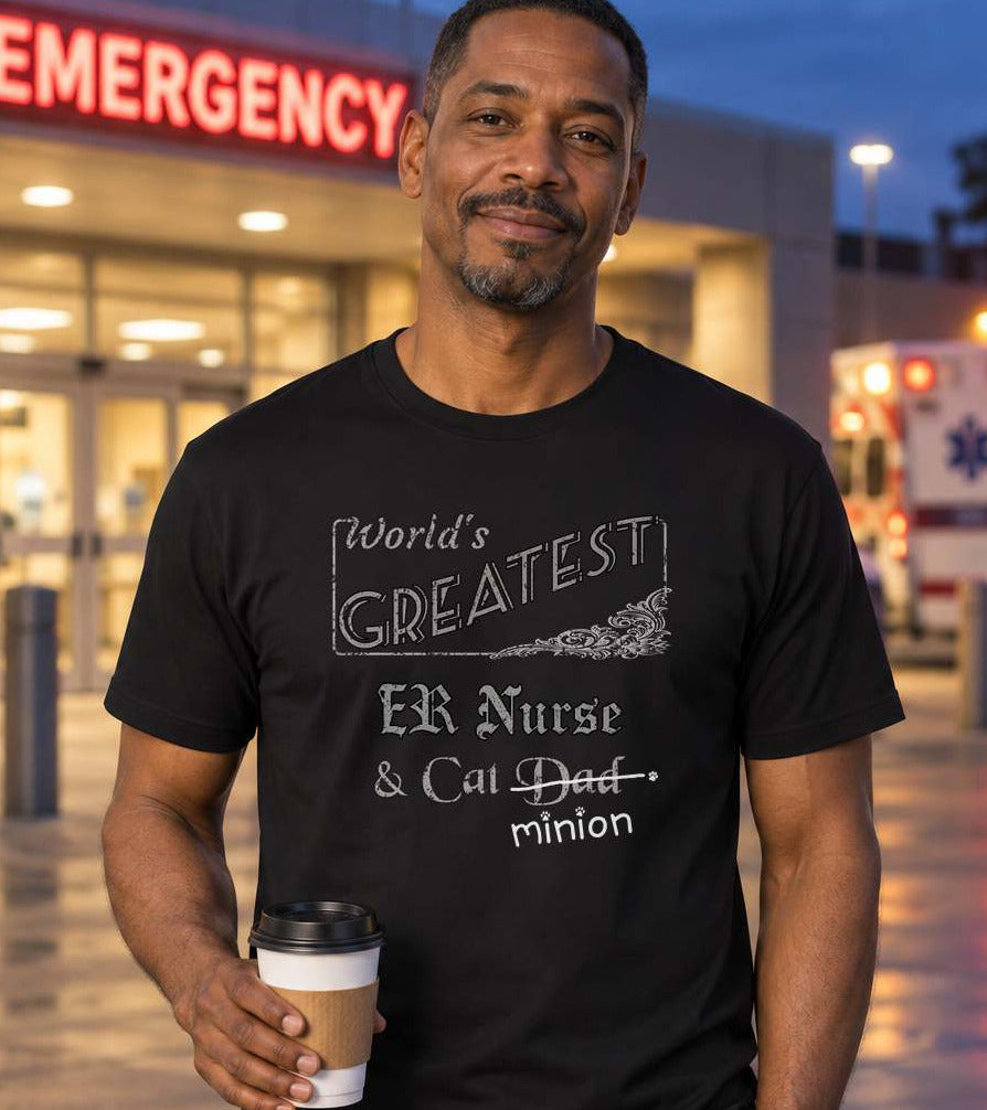 Man holding coffee outside a hospital emergency entrance at dusk, wearing a black crew-neck t-shirt that reads, “World’s Greatest ER Nurse & Cat Dad” with “Dad” crossed out and “minion” handwritten below with paw prints.