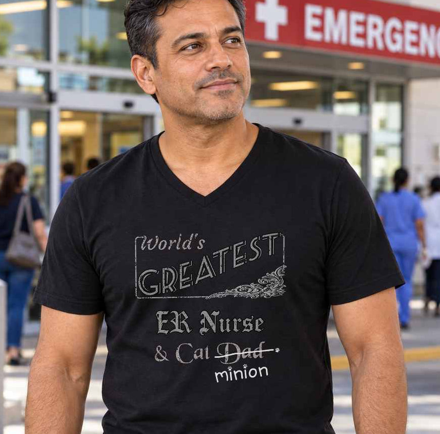 Man standing outside a hospital emergency entrance, wearing a black V-neck T-shirt reading “World’s Greatest ER Nurse & Cat Dad.” “Dad” is crossed out, with “minion” handwritten beneath it and surrounded by cat paw prints.