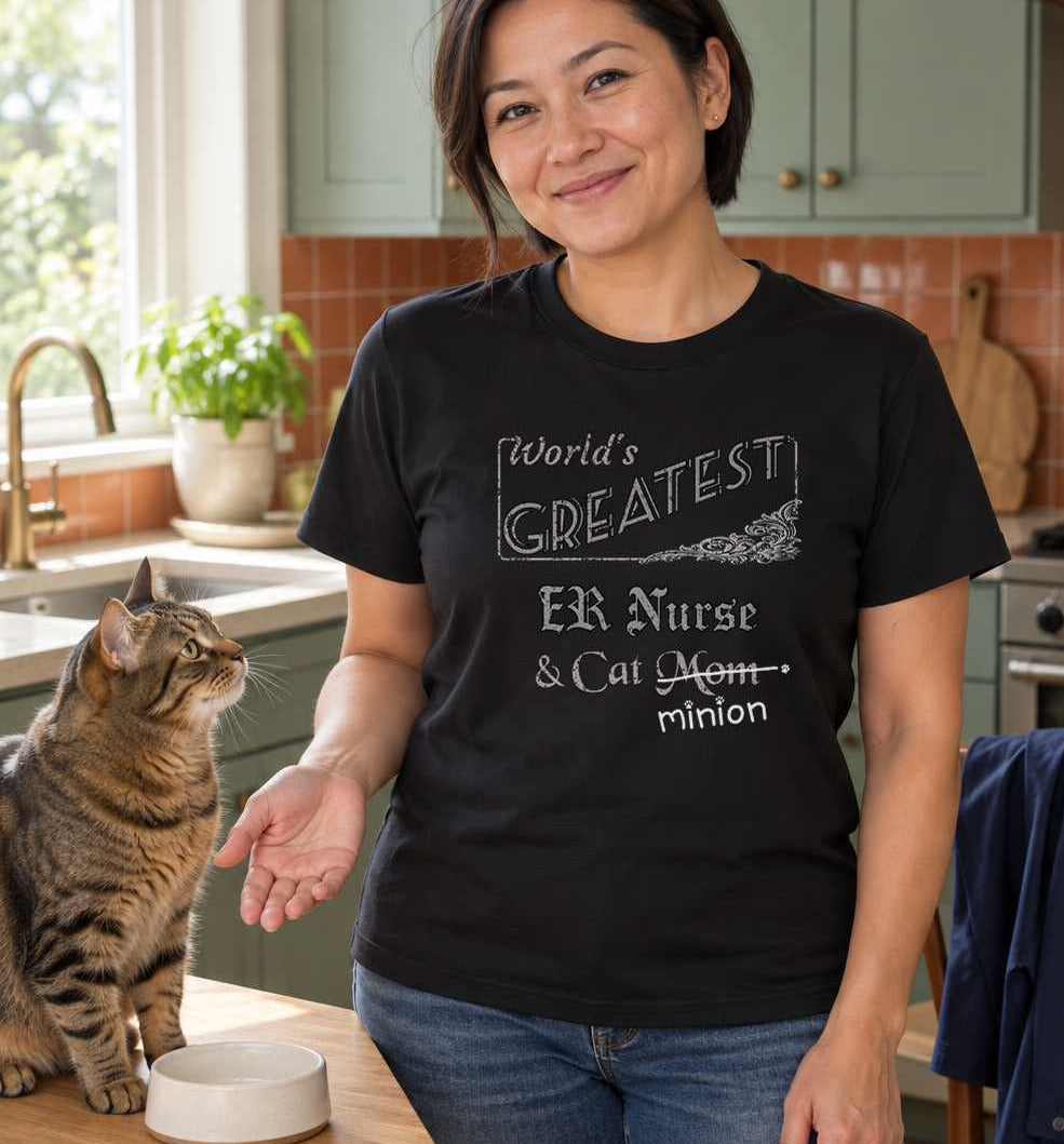 Woman standing beside a waiting cat and food bowl in a kitchen, wearing a black crew-neck t-shirt that reads, “World’s Greatest ER Nurse & Cat Mom” with “Mom” crossed out and “minion” handwritten below with paw prints.