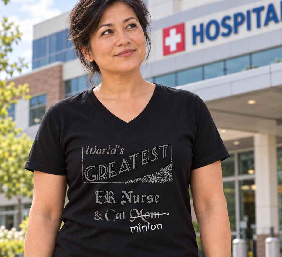 Woman standing outside a hospital emergency entrance, wearing a black V-neck T-shirt reading “World’s Greatest ER Nurse & Cat Mom.” “Mom” is crossed out, with “minion” handwritten beneath it and surrounded by cat paw prints.