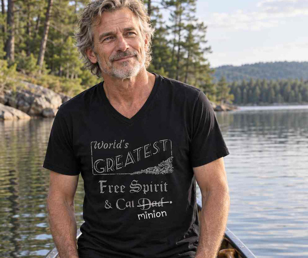 Man kneeling in a canoe on a lake, wearing a black V-neck T-shirt reading “World’s Greatest Free Spirit & Cat Dad.” “Dad” is crossed out, with “minion” handwritten beneath it and surrounded by cat paw prints.