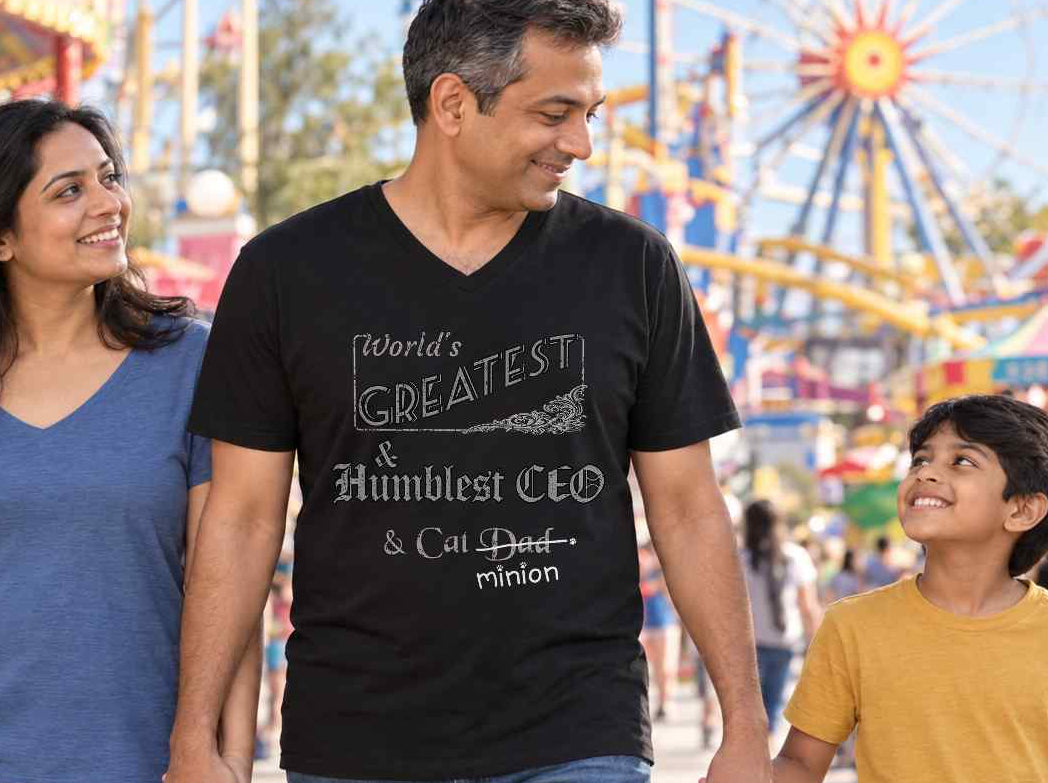 Man walking with his family at an amusement park, wearing a black V-neck T-shirt reading “World’s Greatest & Humblest CEO & Cat Dad.” “Dad” is crossed out, with “minion” handwritten beneath it and surrounded by cat paw prints.