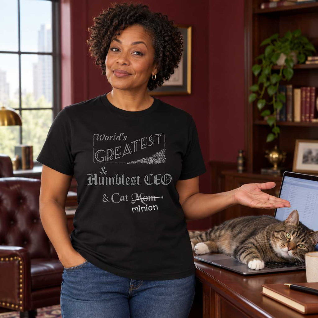 Woman presenting a cat sprawled across a laptop in an office, wearing a black crew-neck t-shirt that reads, “World’s Greatest & Humblest CEO & Cat Mom” with “Mom” crossed out and “minion” handwritten below with paw prints.