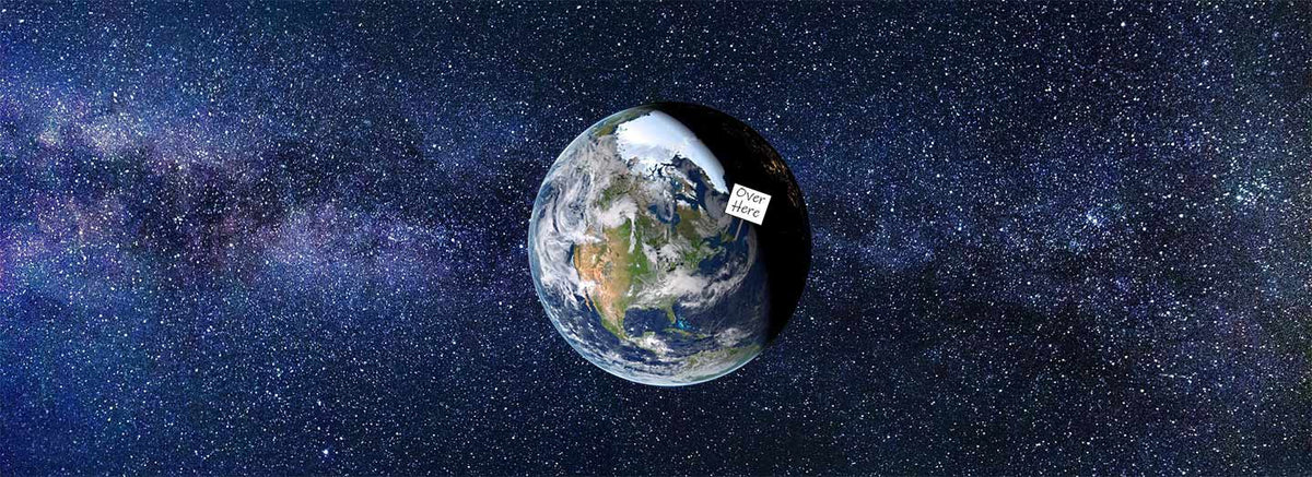 Earth,shown against a star-filled space background with the Milky Way. A small white rectangular sign sticking out of the Earth over Newfoundland that says, "Over Here". The caption along the top edge says, "From a Designer with questionable taste..." and along the bottom edge, "T-Shirts for people who see the world a little differently."