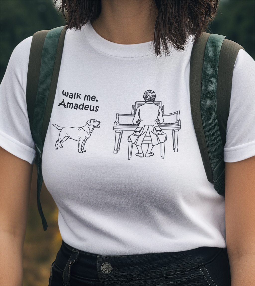 A person wearing a white short-sleeve T-shirt with a black line-art graphic of a dog next to the text 'walk me, Amadeus' and an illustration of a person playing a piano.