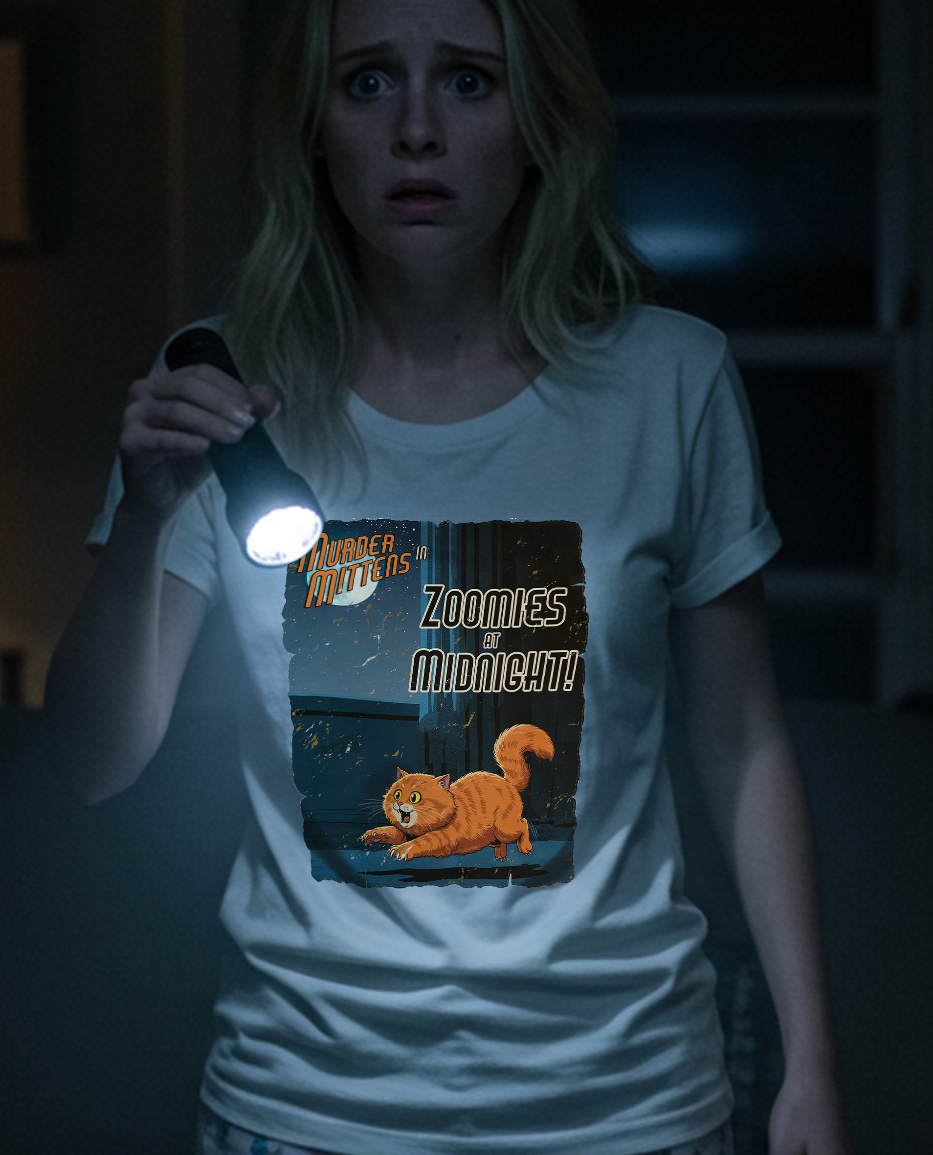A woman in a white t-shirt holding a flashlight, showing a glowing graphic on the front that reads 'Murder Mittens in Zoomies at Midnight!' with an orange tabby cat illustration.